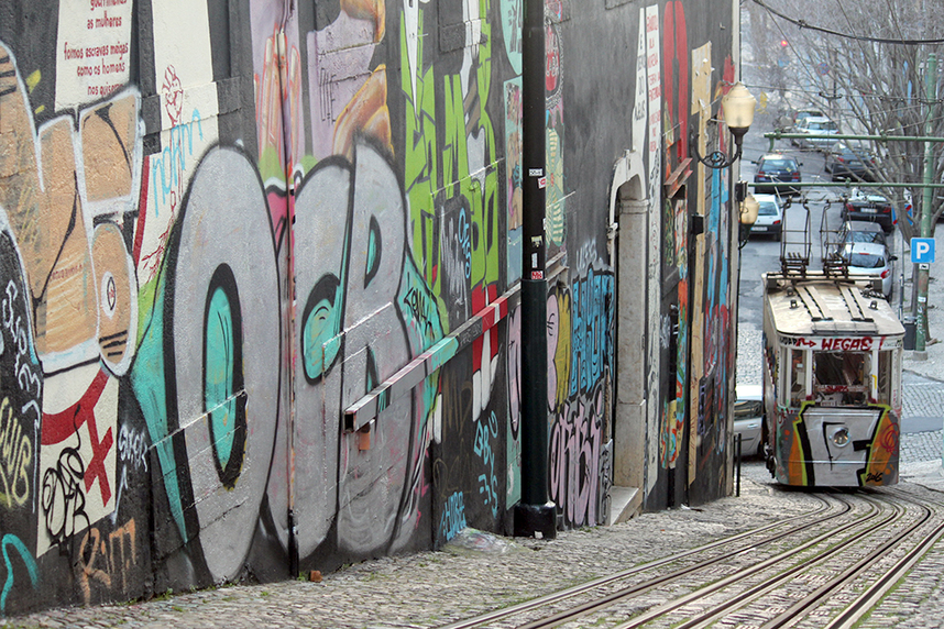 The Ascensor do Lavra tram travelling up the street art and graffiti covered incline of Calçada do Lavra, Lisbon, Portugal.