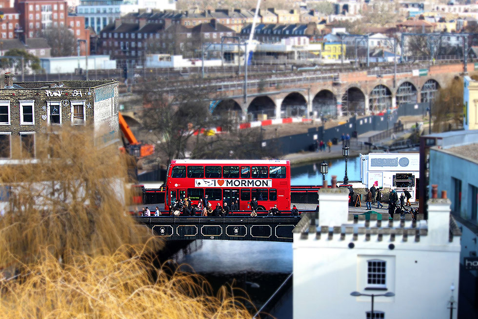A red double decker bus on Camden High Street, crossing Camden Lock, with the now demolished and soon to be redeveloped Camden Lock Village in the background - Camden Town, London England - Tily Travels.