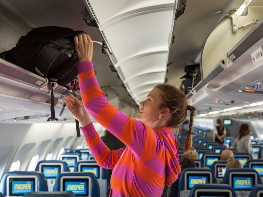 Girl placing a bag in the overhead compartment on a plane.