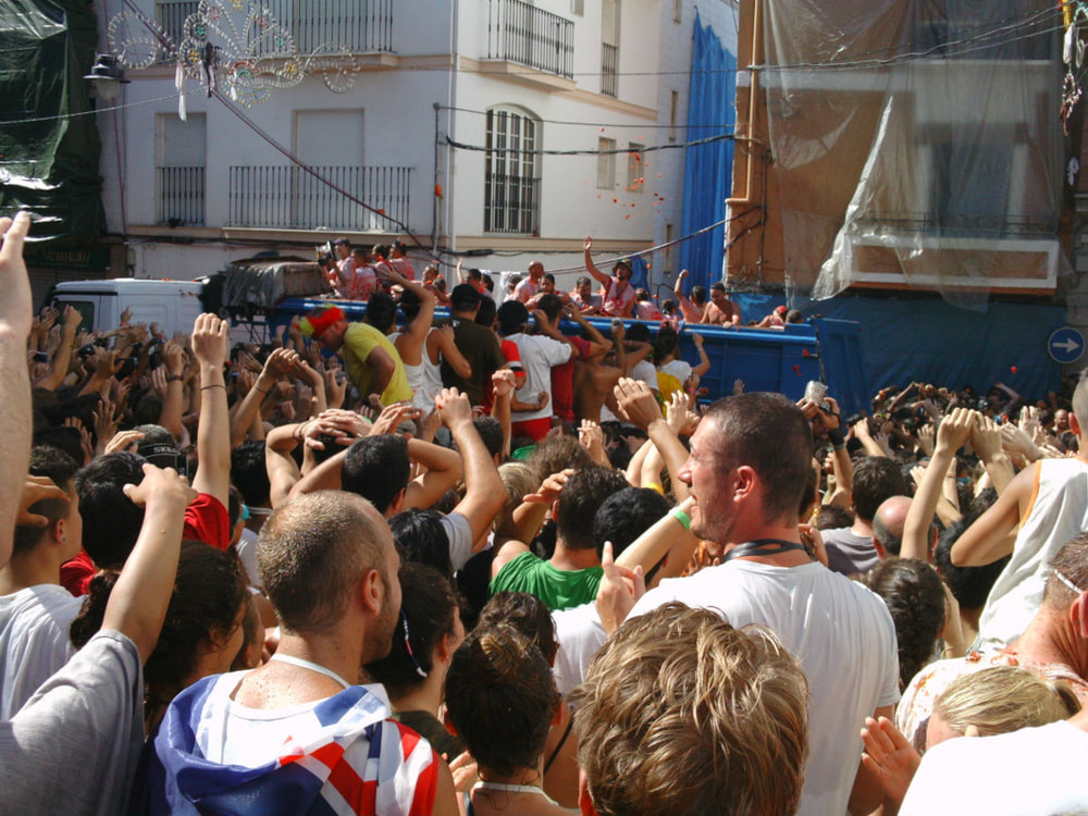 A truck drives Calle Cid and people disperse tomatoes to the awaiting crowd. La Tomatina 2012