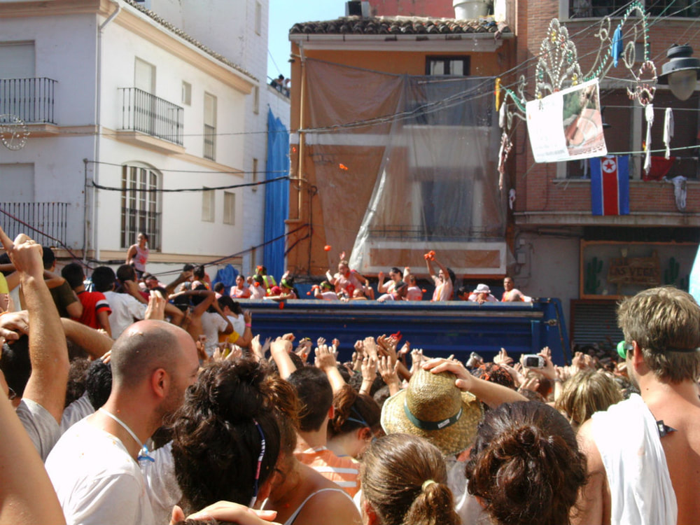 A truck drives Calle Cid and people disperse tomatoes to the awaiting crowd. La Tomatina 2012