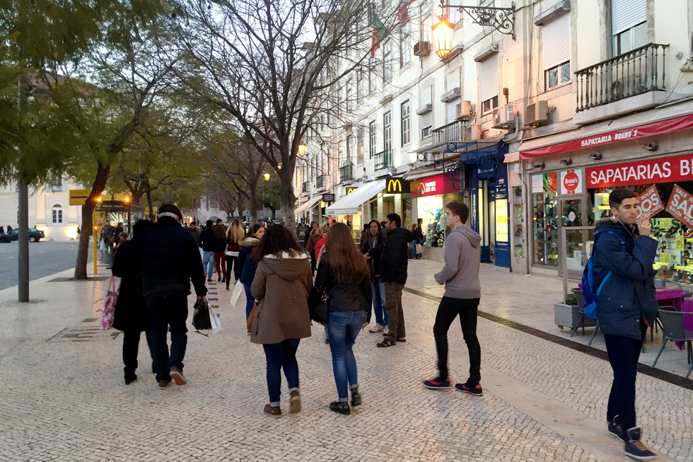 Pedestrians walking in Pedro IV/ Rossio Square past shops and restaurants in Lisbon, Portugal.